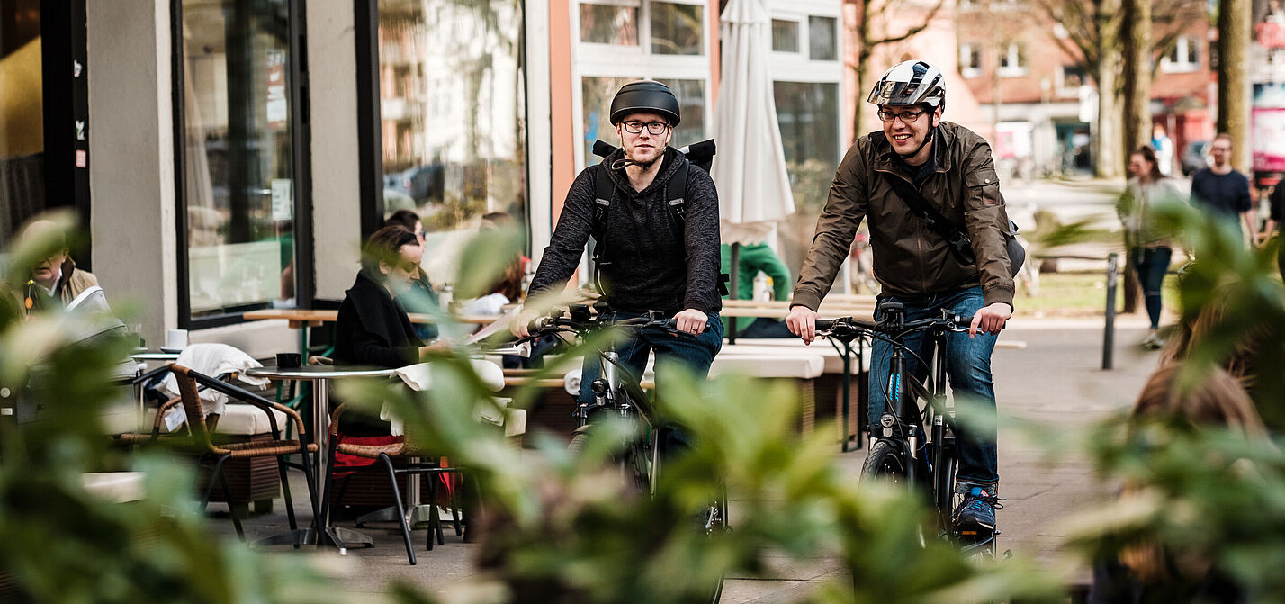 Radfahrer mit Helm Zwei Männer mit Helm fahren auf einem Radweg im urbanen Raum
